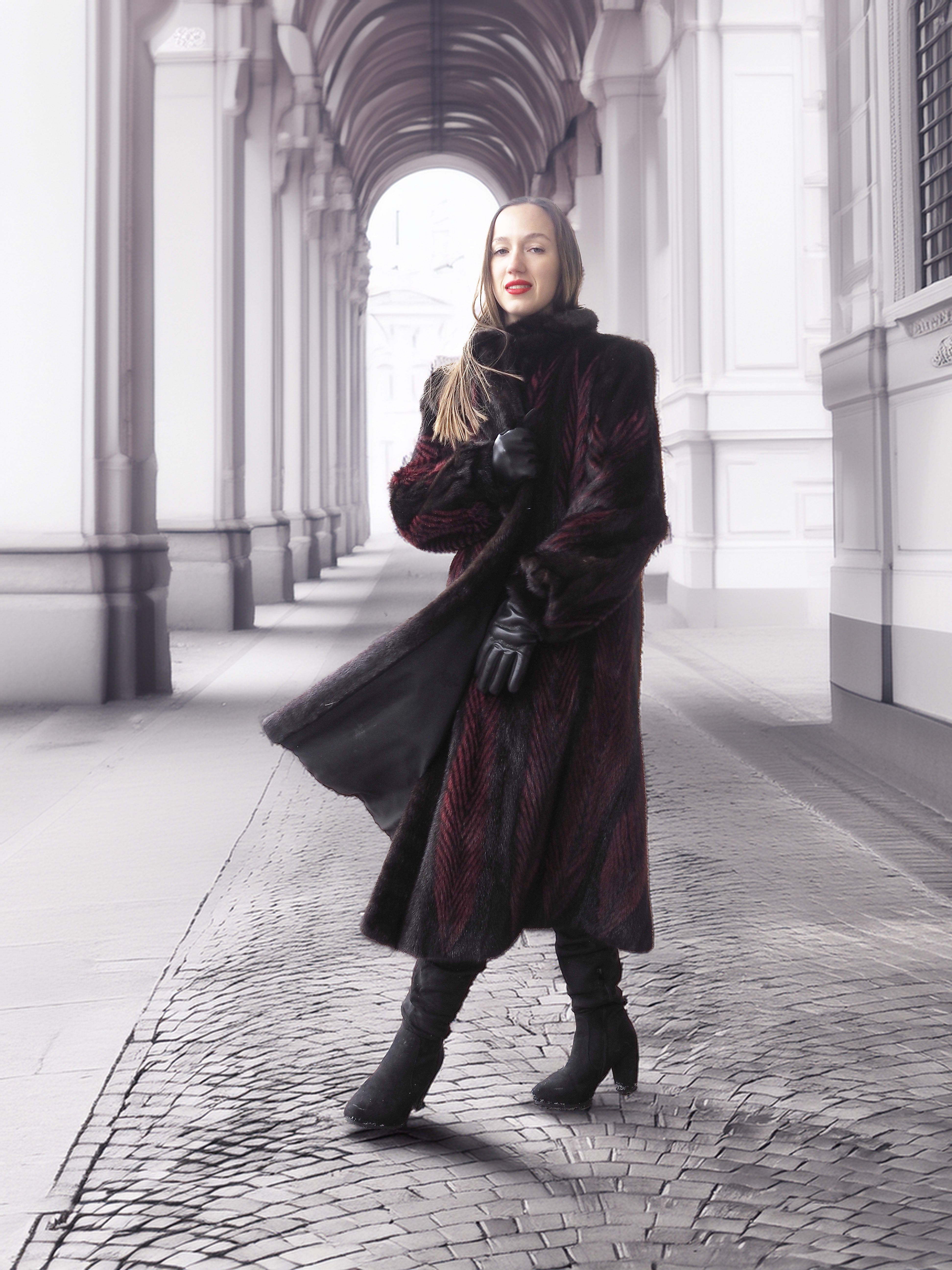 Model poses under archway in red and black mink fur coat, highlighting timeless elegance and fur craftsmanship.