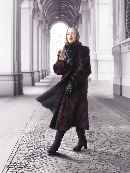 Model poses under archway in red and black mink fur coat, highlighting timeless elegance and fur craftsmanship.