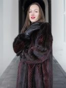 Model poses with gloved hand in red and black mink fur coat, emphasizing plush texture and luxury craftsmanship.