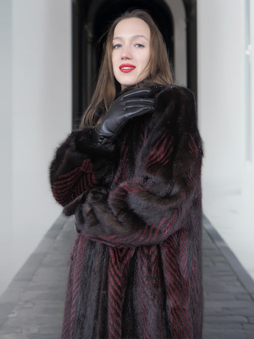 Model poses with gloved hand in red and black mink fur coat, emphasizing plush texture and luxury craftsmanship.