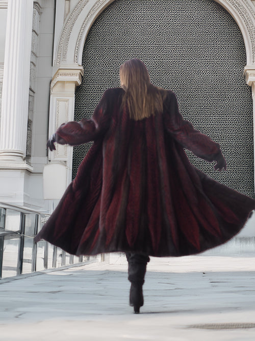 Back view of flowing two tone mink fur coat in red and black, showcasing full-length design and dramatic movement.