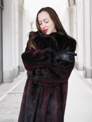 Model hugs herself in red and black mink fur coat, highlighting warmth and comfort of luxury winter outerwear.