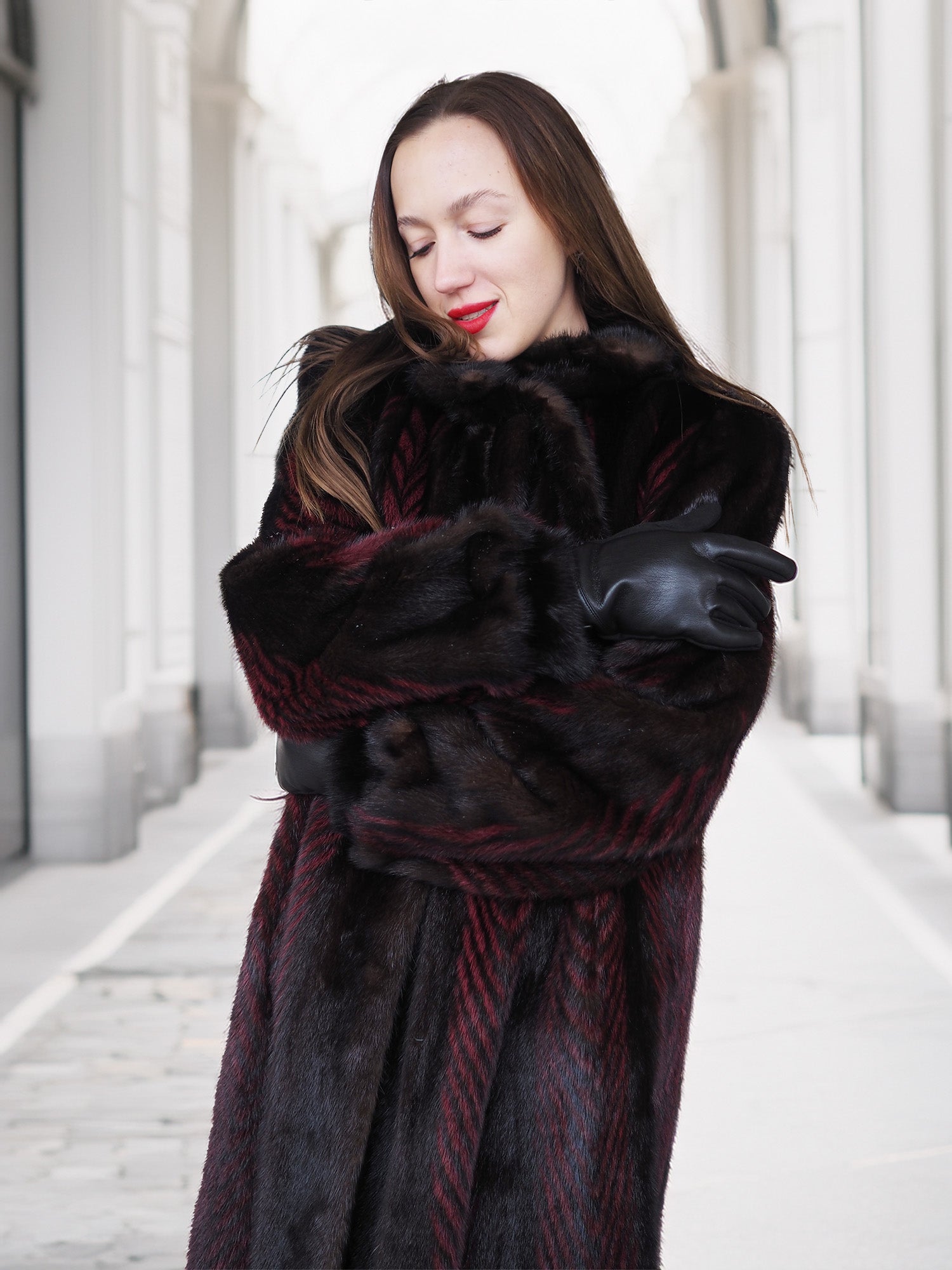 Model hugs herself in red and black mink fur coat, highlighting warmth and comfort of luxury winter outerwear.
