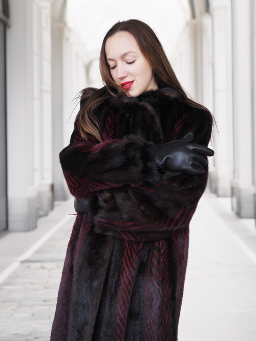 Model hugs herself in red and black mink fur coat, highlighting warmth and comfort of luxury winter outerwear.
