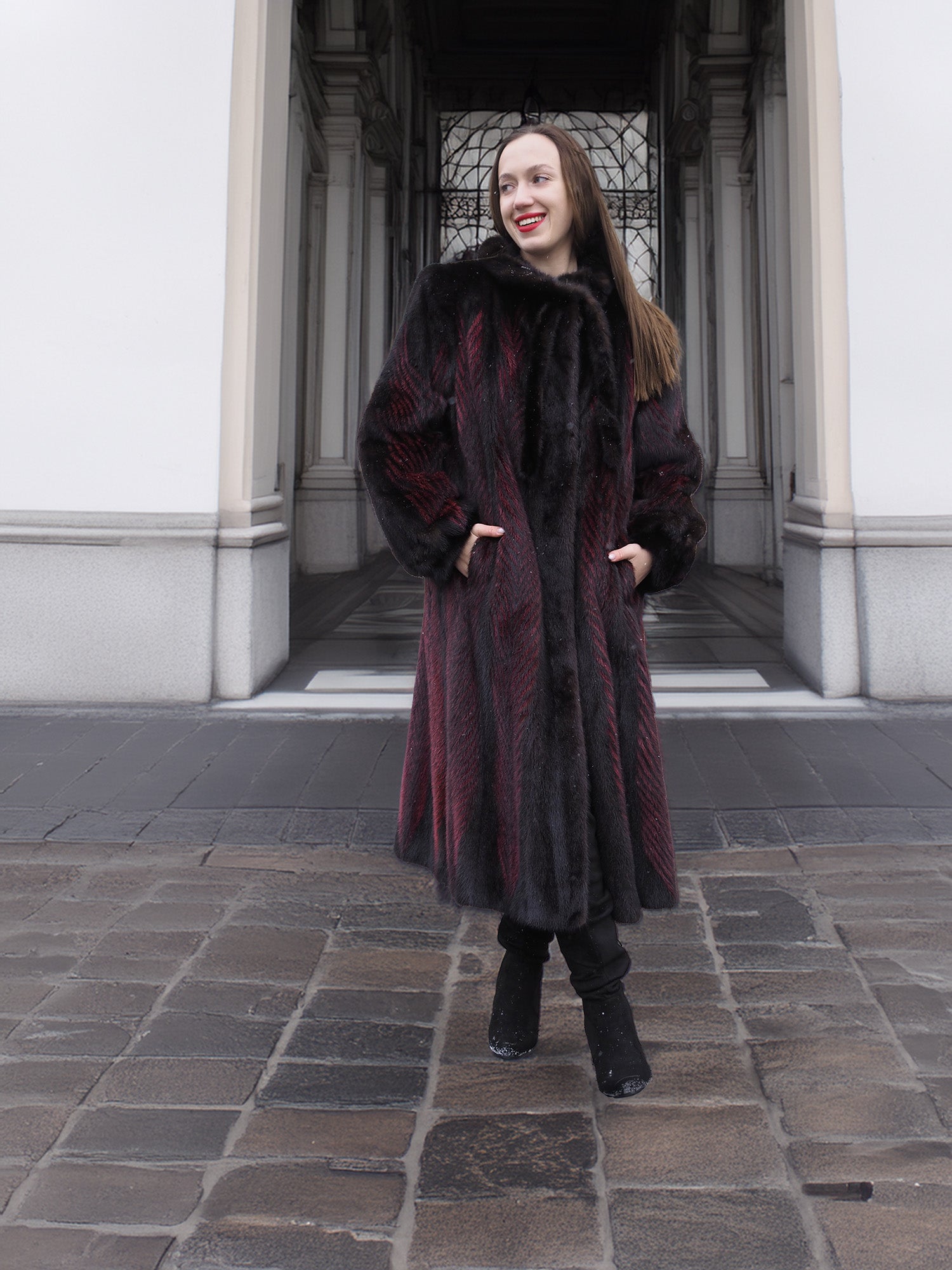 Smiling model wears red and black mink fur coat with hands in pockets, ideal for elegant winter outerwear styling.