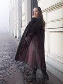 Model glances over shoulder in red and black mink fur coat, showcasing sustainable and stylish winter outerwear.