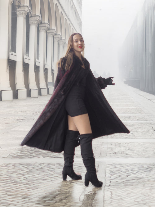Model twirls in open red and black mink fur coat, revealing black mini dress for bold winter fashion statement.