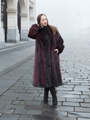 Model poses in red and black mink fur coat on cobblestone street, showcasing luxurious and warm full-length outerwear.