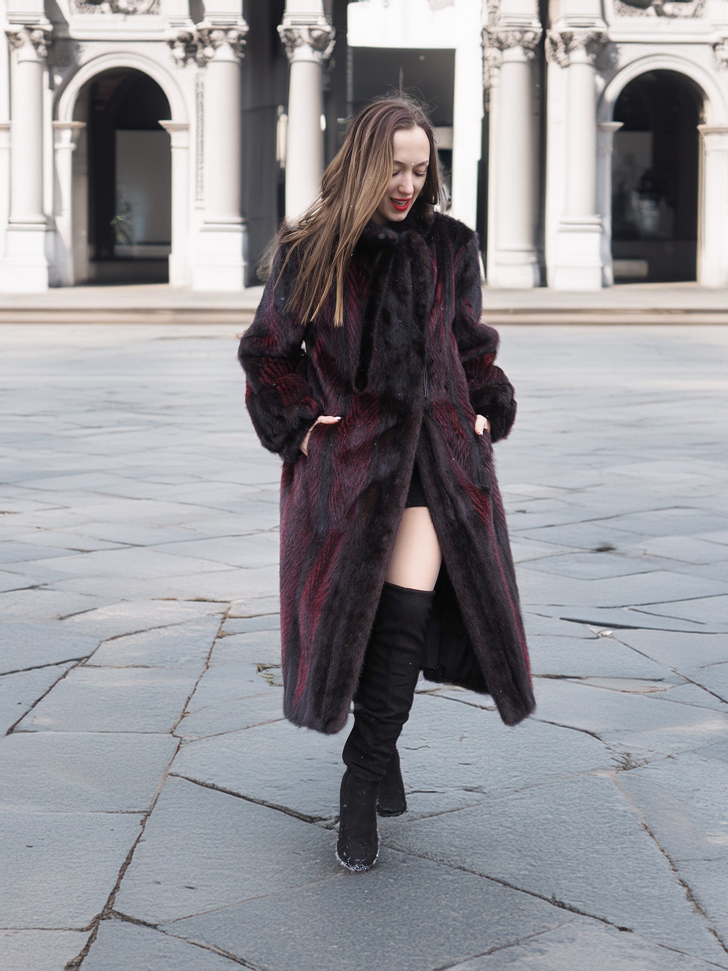Model walks confidently in red and black mink fur coat, highlighting its unique two-tone design and luxurious texture.