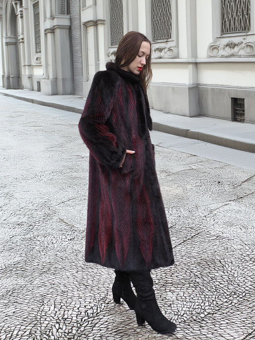 Model walks along textured pavement in red and black mink fur coat, highlighting its elegant and sustainable design.