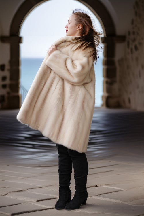 Pearl mink swing coat with hood, cream fur, full flared hem over tall boots