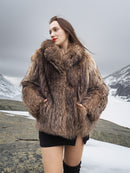 Model wearing Raccoon Glamour Jacket - Mountain Mirage S/M in snowy terrain, highlighting real raccoon fur and plush collar design.