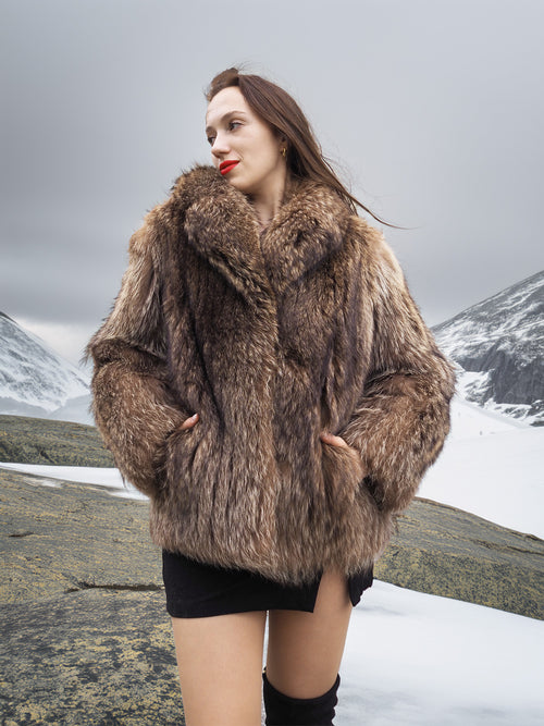 Model wearing Raccoon Glamour Jacket - Mountain Mirage S/M in snowy terrain, highlighting real raccoon fur and plush collar design.