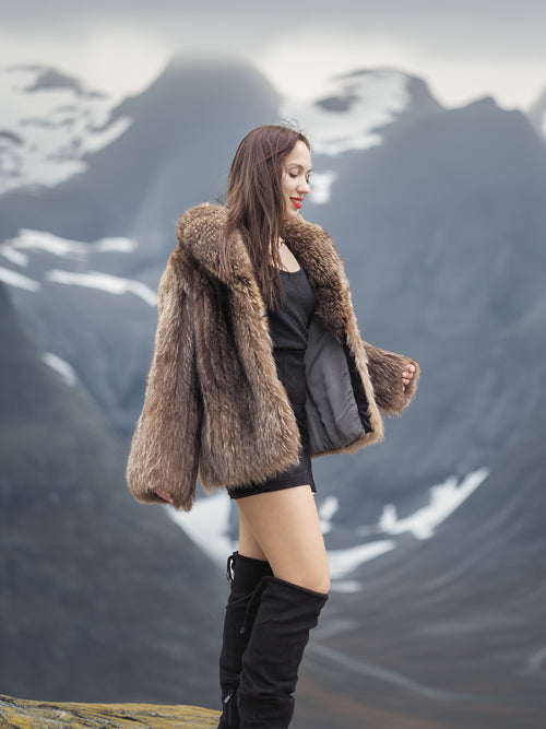 Side view of Raccoon Glamour Jacket - Mountain Mirage S/M in alpine setting, emphasizing fur volume and stylish silhouette.