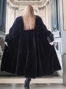 Person wearing a long black fur coat in an elegant interior setting