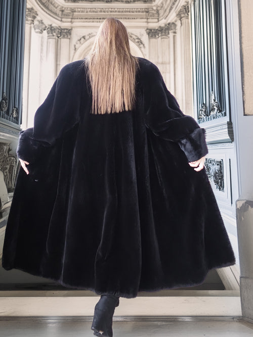 Person wearing a long black fur coat in an elegant interior setting