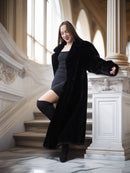 Woman in a black coat standing on a staircase in an elegant interior setting