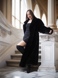 Woman in a black coat standing on a staircase in an elegant interior setting