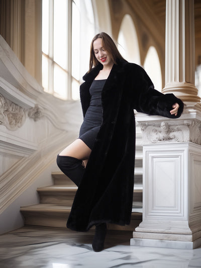 Woman in a black coat standing on a staircase in an elegant interior setting