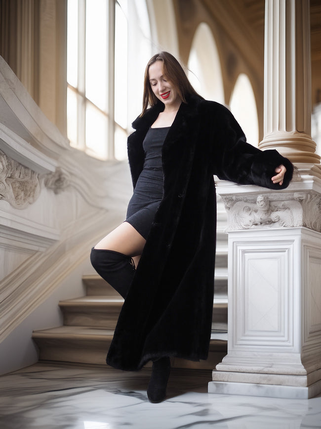 Woman in a black coat standing on a staircase in an elegant interior setting