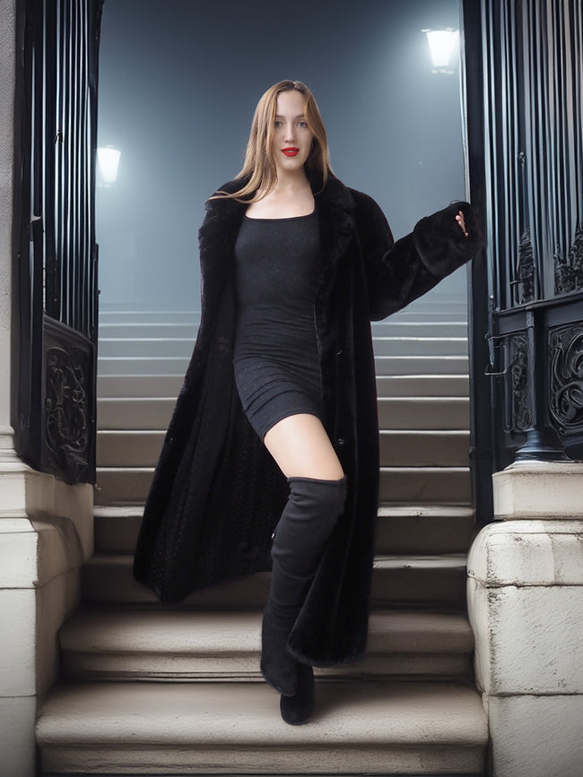 Woman in a long black coat and knee-high boots standing on steps at night.