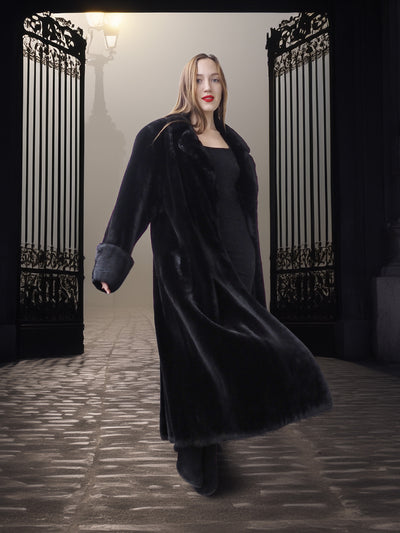 Woman wearing a long black coat in an elegant setting with decorative gates.