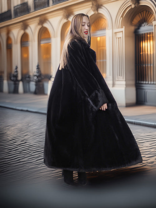 Woman wearing a long black coat in an urban setting with classical architecture.