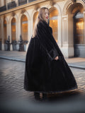 Woman wearing a long black coat in an urban setting with classical architecture.