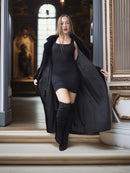 Woman in a black coat and dress standing in an elegant interior setting