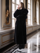 Woman in a black coat standing in an elegant interior setting with marble floors and gold accents.