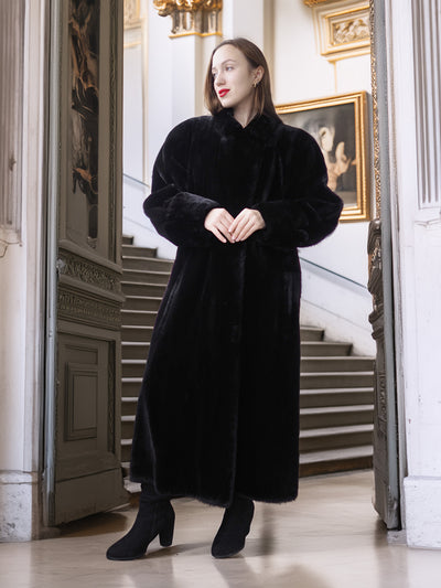 Woman wearing a long black coat in an elegant interior setting