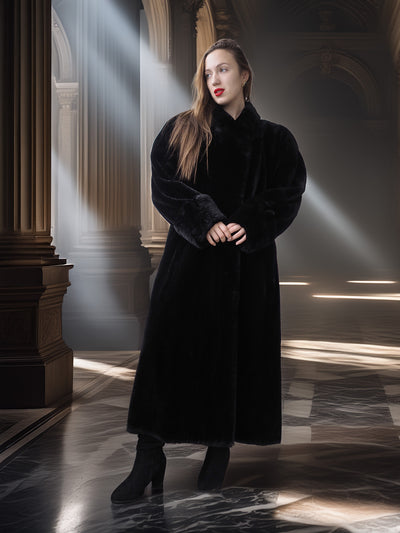 Woman in a long black coat standing in a dimly lit, architecturally detailed room.