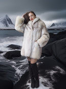 Person wearing a fur coat standing in a snowy landscape with mountains.
