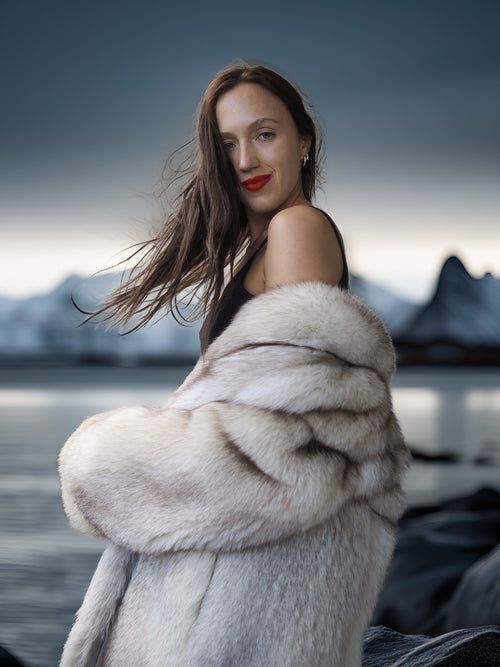 Woman in a fur coat standing in front of a mountainous landscape