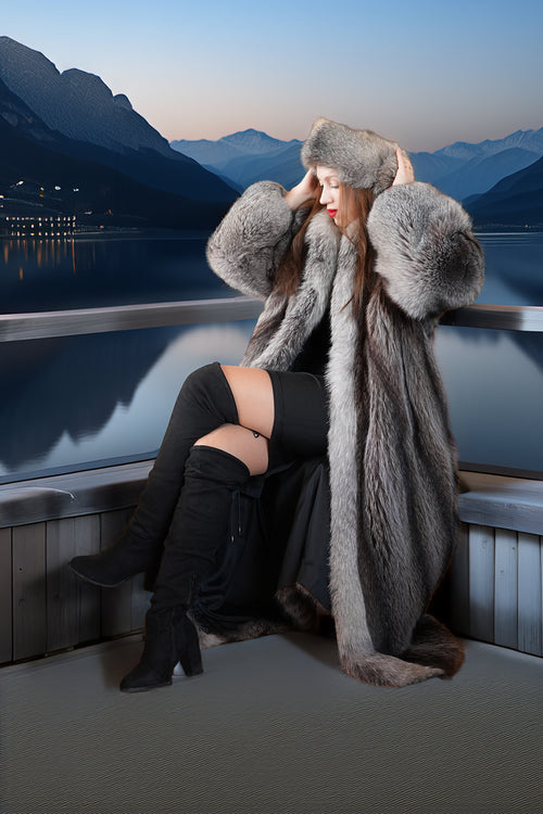 Woman in a fur coat sitting by a scenic mountain lake.