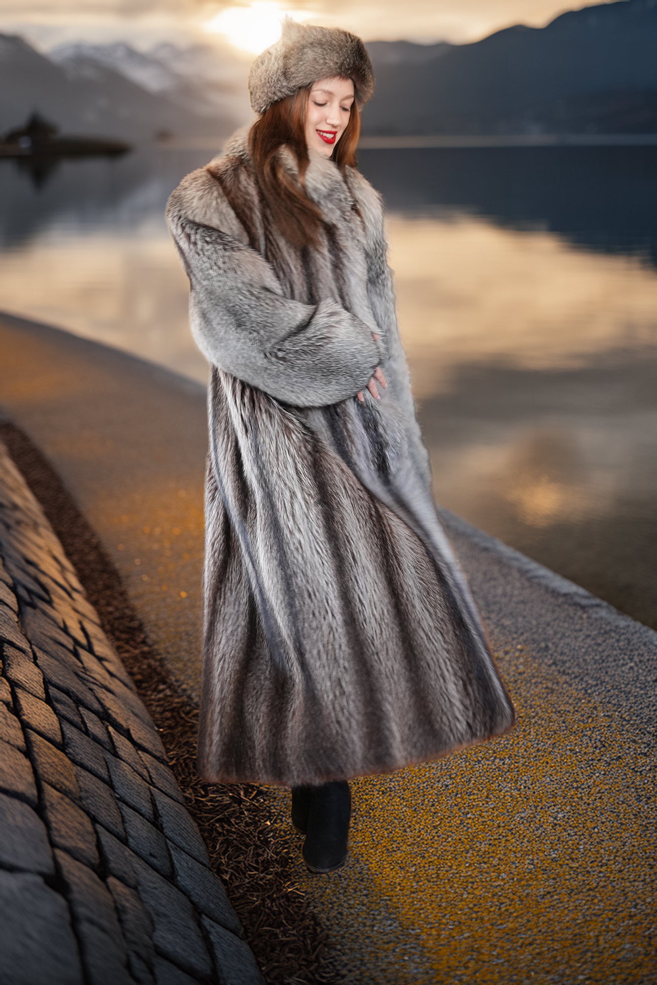 Woman in a fur coat standing by a lake with mountains in the background