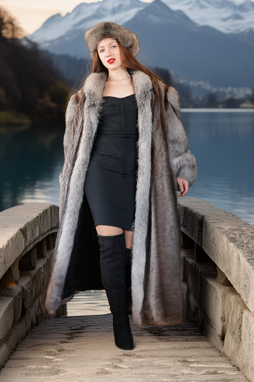 Woman in a fur coat and hat standing on a wooden bridge with mountains in the background