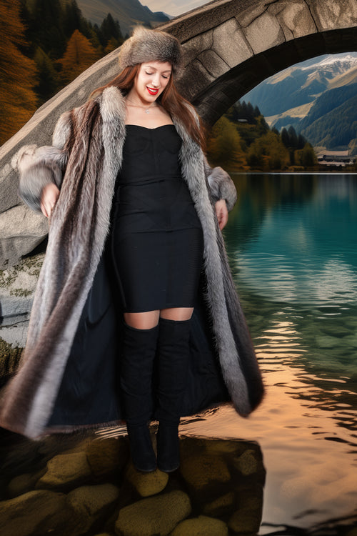 Woman in a long fur coat standing by a lake with mountains in the background