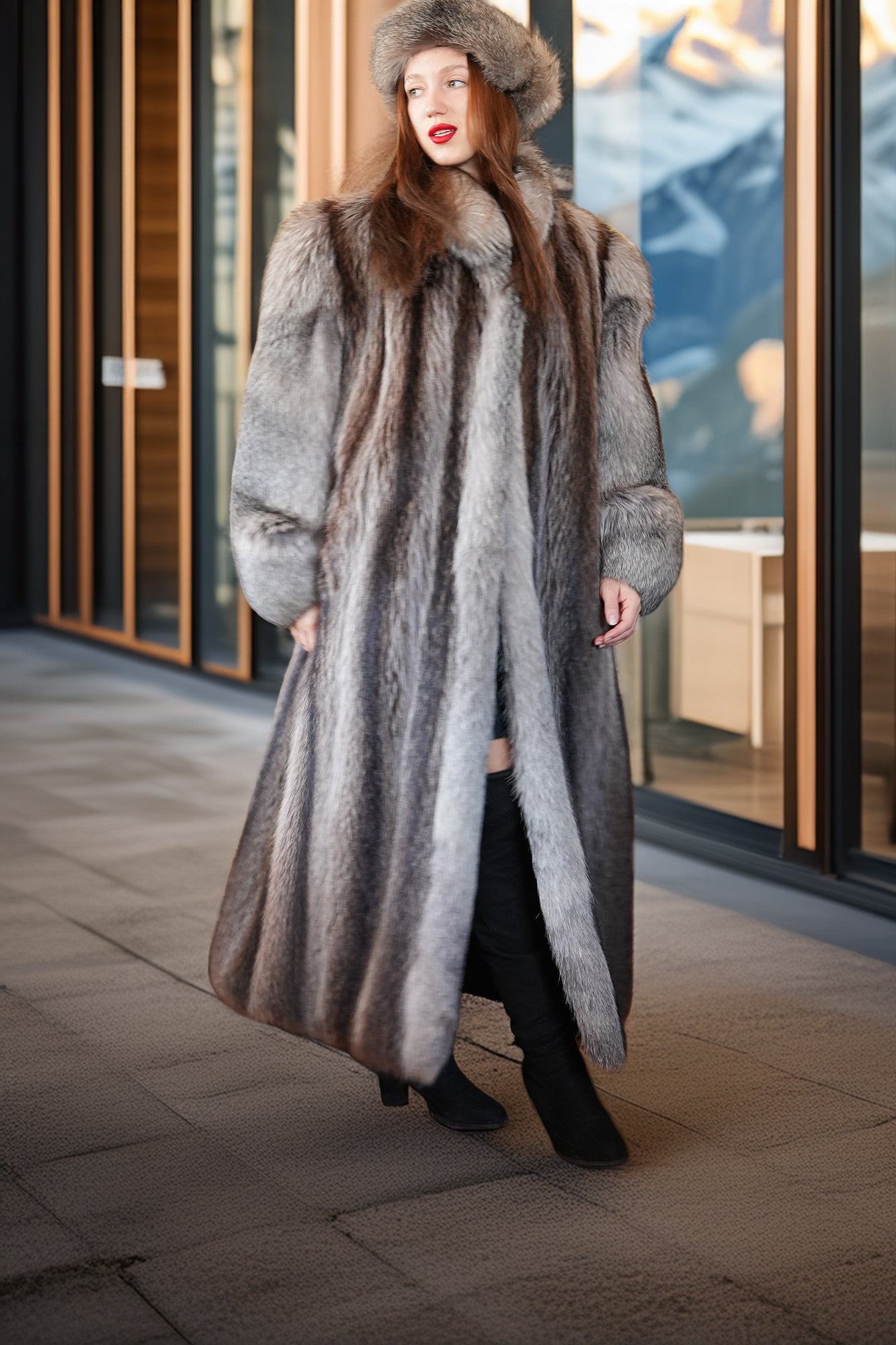 Woman wearing a fur coat and hat standing in front of a glass door with mountain view.