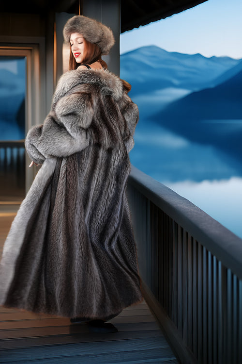 Woman in a fur coat standing on a balcony with a scenic view of mountains and water.