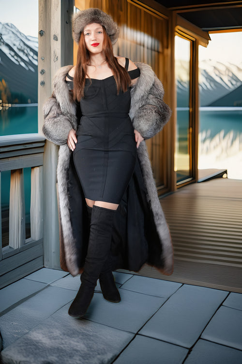 Woman in a fur coat standing on a deck with mountains and water in the background