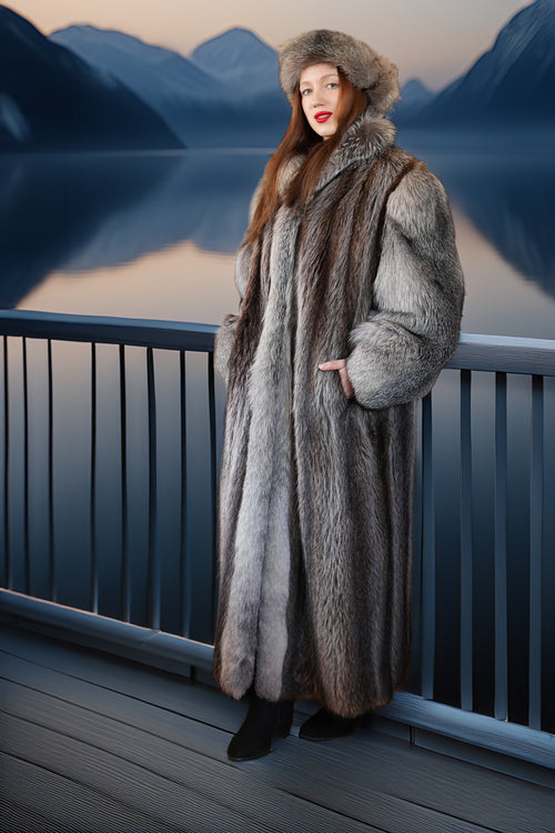Woman in a fur coat standing on a deck with mountains and water in the background