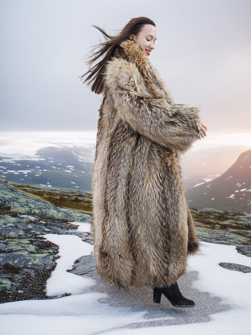 Side view of Finnish Raccoon Fur Coat with natural brown tones and shawl collar, worn in snowy mountain landscape.