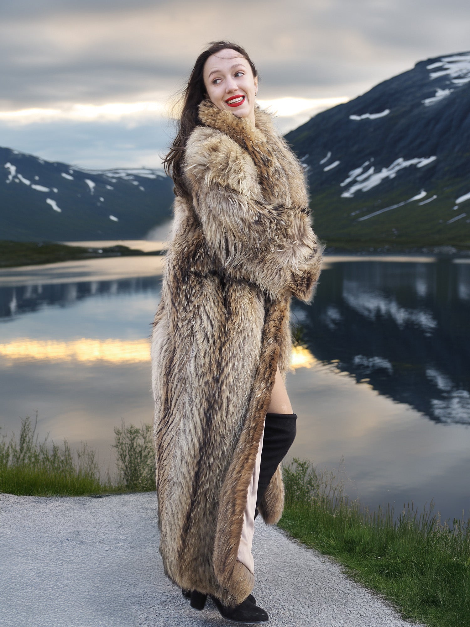 Model smiling in Finnish Raccoon Fur Coat with flowing hem and plush collar, styled for luxury winter fashion by a lake.