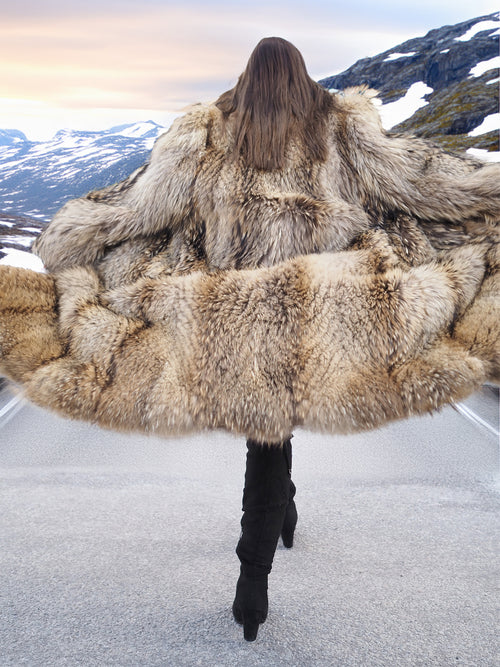 Back view of Finnish Raccoon Fur Coat in motion, showcasing expansive fur volume and dramatic silhouette on mountain road.