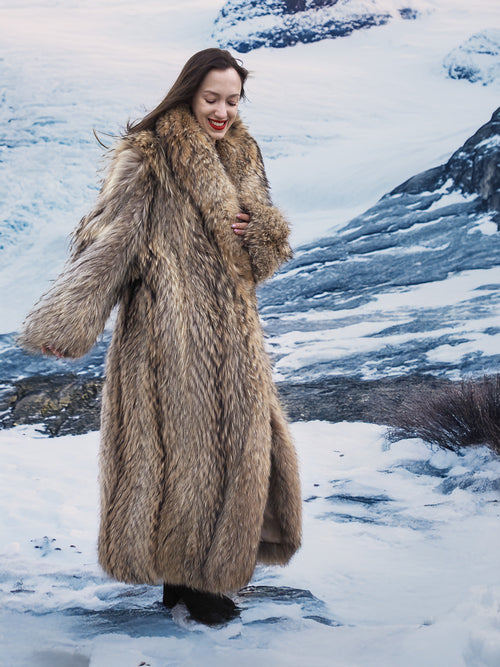 Model walking in snow wearing Finnish Raccoon Fur Coat with thick collar and full-length design, ideal for winter warmth.