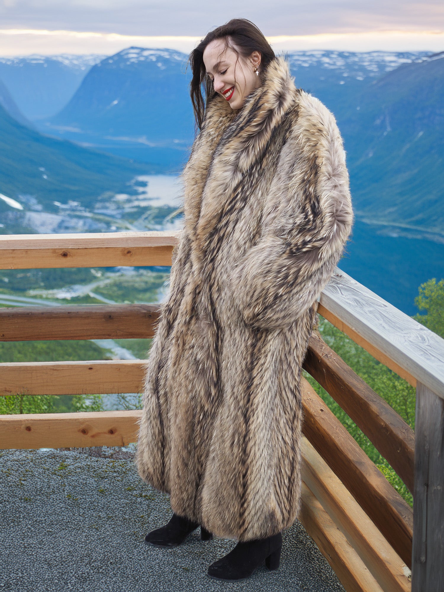 Model leaning on wooden railing in Finnish Raccoon Fur Coat, showcasing luxurious fur texture and elegant winter style.