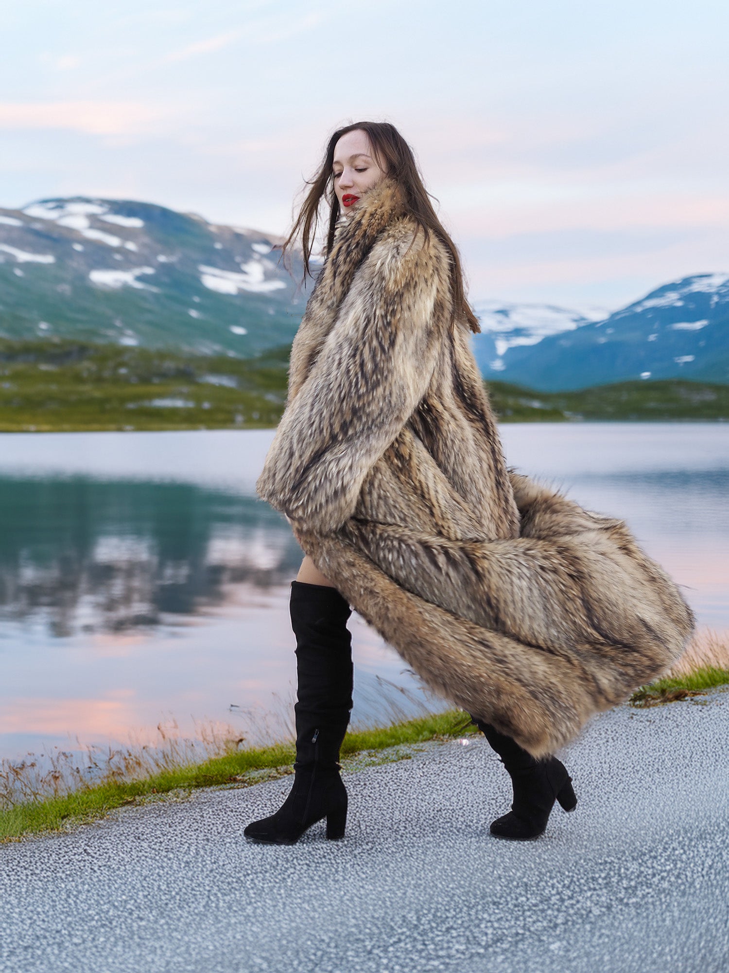 Model walking in Finnish Raccoon Fur Coat with flowing hem and shawl collar, styled with thigh-high boots in alpine setting.