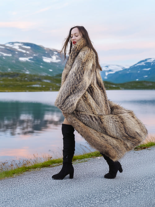 Model walking in Finnish Raccoon Fur Coat with flowing hem and shawl collar, styled with thigh-high boots in alpine setting.