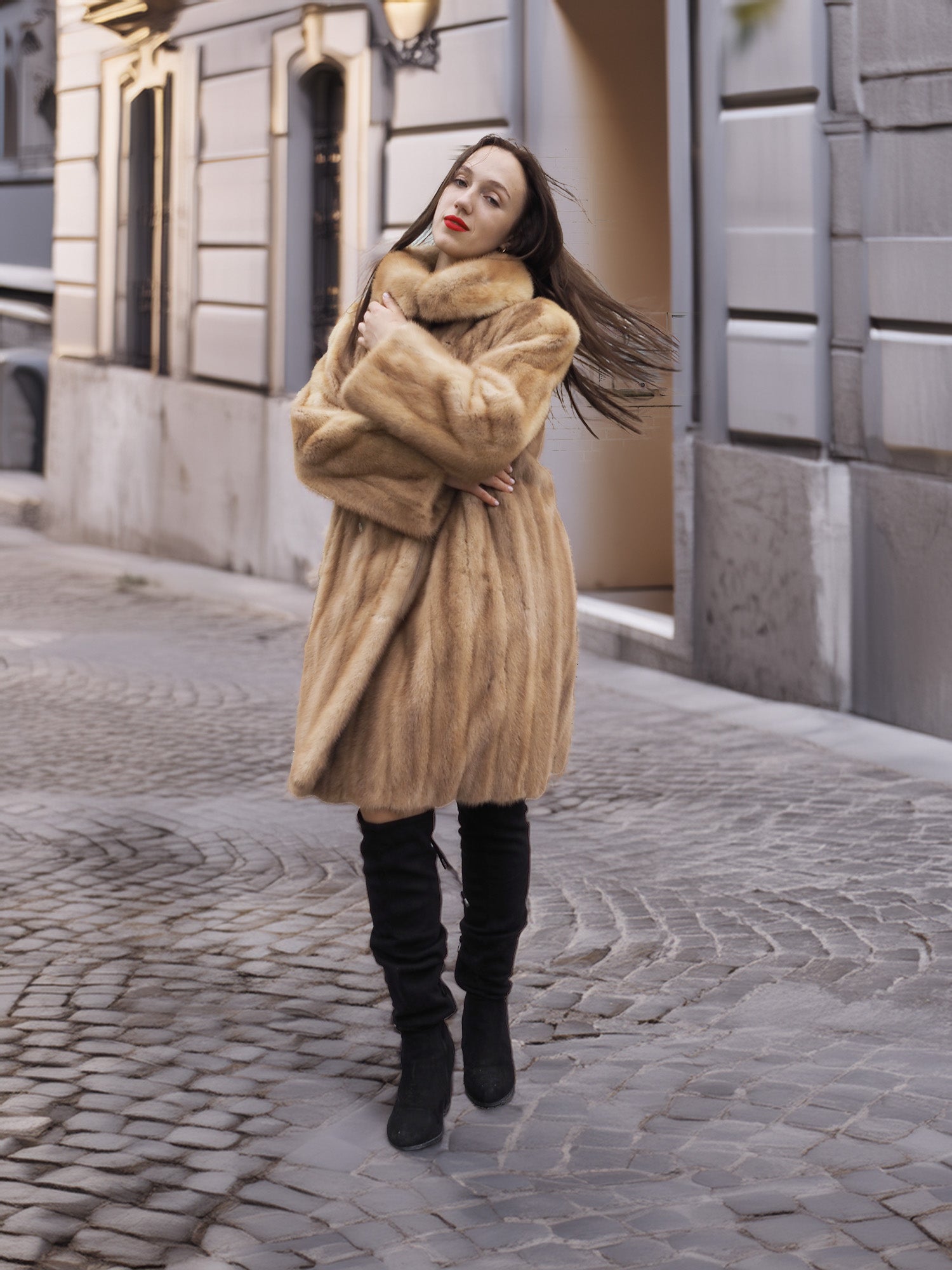 Golden Reverie M - Cozy blond mink coat with high collar, styled for winter elegance on a cobblestone street.